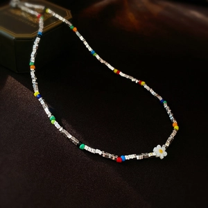 Détail de perles colorées et d'un pendentif fleur blanche sur un collier ras du cou