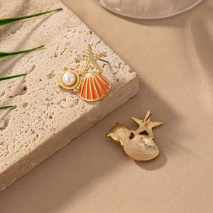 Macro shot of seashell and starfish earrings with pearls on beach sand texture