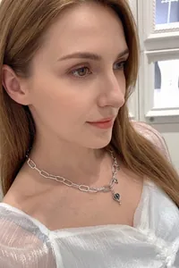 Close-up of a silver chain necklace with a heart-shaped blue gemstone pendant on a model
