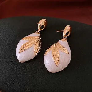 Golden drop leaf earrings with white marble enamel finish shown on a dark jewelry stand