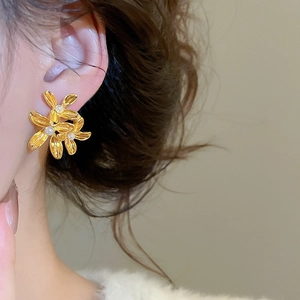Close-up of gold flower stud earrings with white pearls worn on a female model