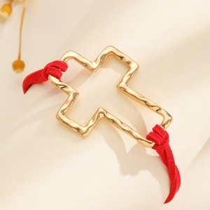Detailed shot of golden hollow cross charm with hammered texture on red cord bracelet