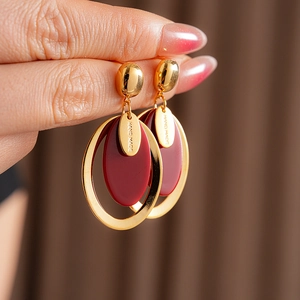 Detailed shot of handmade gold-plated oval resin earrings worn by a model in burgundy red