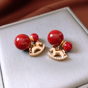 Detail of red bead earrings with golden rocking horse pendant and crystal inlay