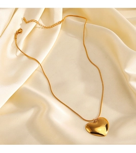 Macro detail of gold heart pendant on snake chain over elegant beige silk fabric