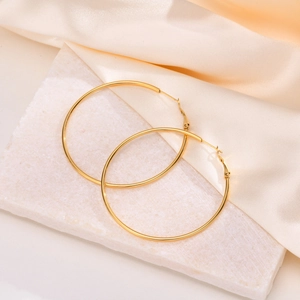 Golden oversized thin hoop earrings displayed on marble and champagne silk background
