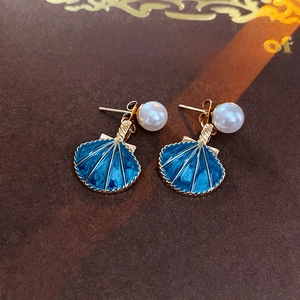 Détail macro de boucles d'oreilles festonnées en émail bleu avec perles blanches et doré