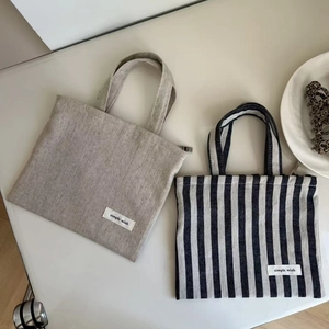 Close-up of oatmeal and navy striped cotton linen mini handbags with Simple Wish tags