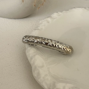 Detailed view of a silver metal hair clip with hammered texture on a ceramic plate