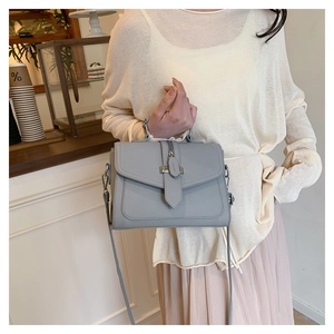 Grey leather flap handbag with metal buckle worn by model in a bright cafe setting