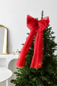 Close-up of a large red mesh bow with long ribbons on top of a lit Christmas tree