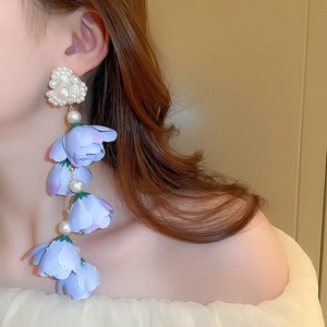 Dettaglio di orecchini a fiori lunghi con petali in tessuto blu e cuore di perle