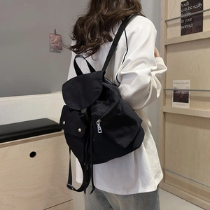 Rear view of model wearing a black nylon drawstring backpack with flap and side pockets