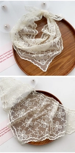 Detail of white lace neckerchief featuring floral embroidery and wavy scalloped edges