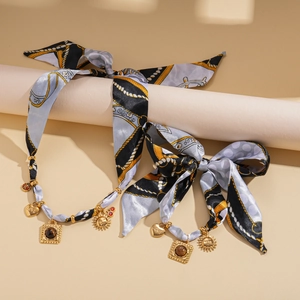 Detail of scarf necklace with gold sun charms and heart pendant on beige stand