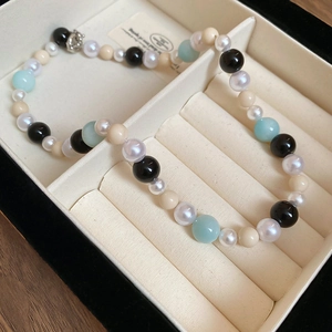 Detail of beaded necklace with mixed blue, black, and cream pearls on white velvet box