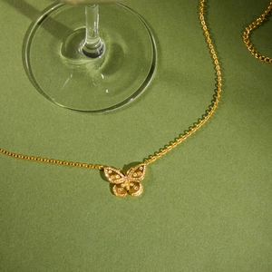 Vue détaillée d'un pendentif papillon doré orné de strass brillants sur fond vert