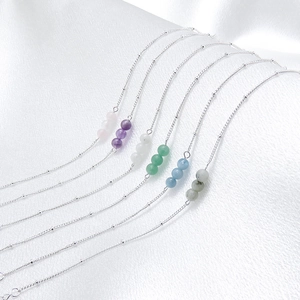 Detail of natural stone beaded bracelets in silver finish on white silk background