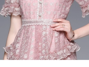 Détail d'une robe en dentelle rose avec broderie florale 3D et boutons de perles