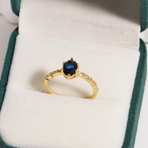 Detailed shot of a gold ring with an oval blue zircon and small side diamonds in a box