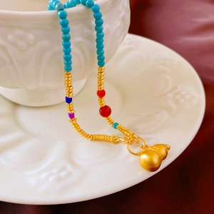 Détail d'un collier pendentif gourde dorée sur porcelaine avec des perles vertes
