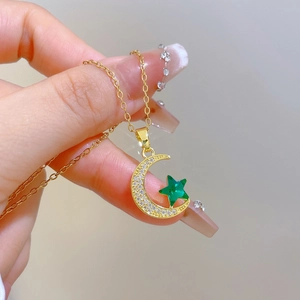 Handheld close-up of gold star and moon necklace with sparkling crystals and green stone