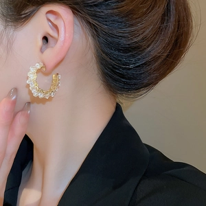 Macro detail of golden C-shaped hoop earrings with crystal beads on a model wearing black