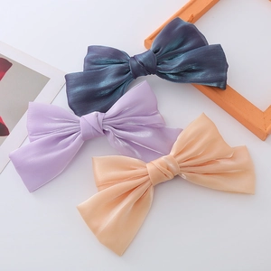 Detailed view of three pearl satin bow hair clips in teal, lilac, and peach colors