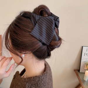 Close-up of a black and white polka dot bow hair clip worn on a brown wavy bun hairstyle