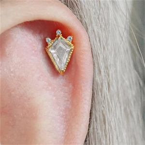 Macro shot of gold kite-shaped stud earring with sparkling diamond accents on ear