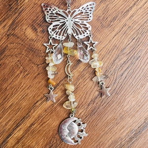 Macro detail of silver suncatcher with crystal beads, moon, and butterfly icons on wood