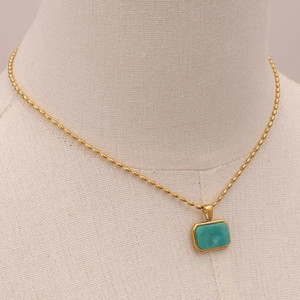 Detail of a gold rice chain necklace with a rectangular turquoise stone on a beige mannequin