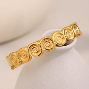 18K gold plated stainless steel spiral bangle with embossed texture on ceramic display