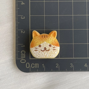 Detailed macro view of a 2.5cm orange resin cat bread charm with scale reference