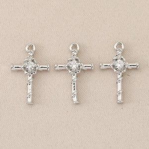 Detail of three silver baroque cross pendants with twisted design and clear gemstone center