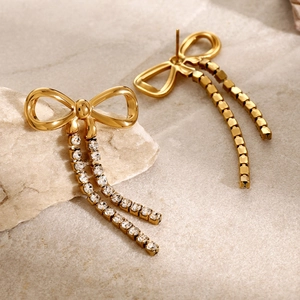 Macro shot of gold bow earrings featuring double rhinestone fringe on natural stone