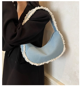 Detail of light blue denim crescent bag featuring white frayed fringe edges and zipper closure