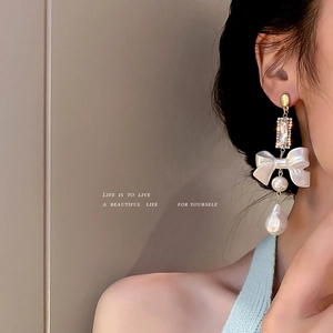 Elegant long gold bow earrings with crystal accents and baroque pearl pendants on a model