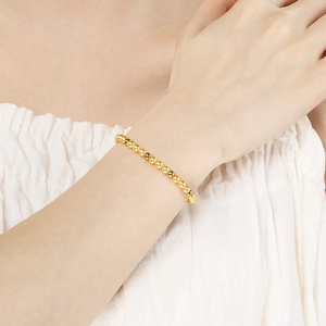 Detailed view of elegant gold beaded bracelet worn on wrist with white fabric background