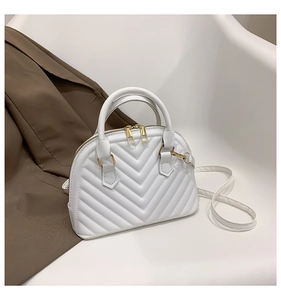 Detail of white quilted shell bag with gold zippers and adjustable shoulder strap