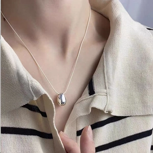 Close-up of a silver teardrop pendant necklace with a polished mirror finish on model