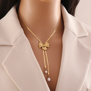 Gold bow pendant necklace with long tassels and pearls shown on a professional model