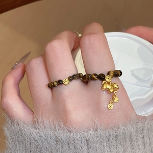 Tiger eye stone bead ring with golden pig and coin charms on a model's hand