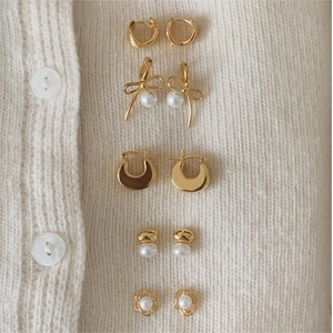 Detail view of five pairs of gold-plated earrings with pearls on white knit fabric