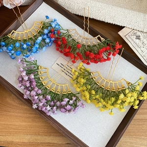 Detail view of four colorful floral hair sticks with wavy golden pins in a wooden tray