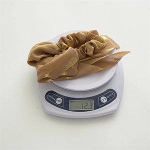 Brown floral chiffon scrunchie with gold feather patterns shown on a digital scale at 12.3g