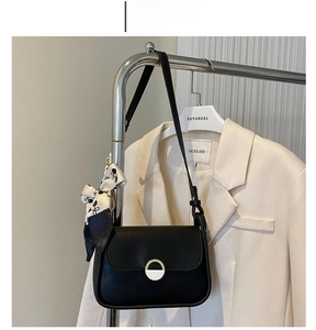 Detail of black matte shoulder bag with gold clasp and decorative silk scarf accessory