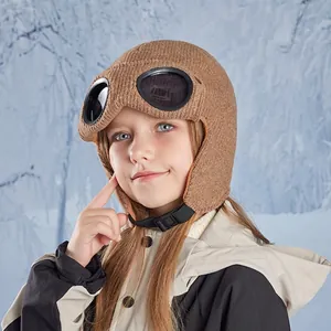 Winter camel knit pilot hat for kids with earflaps and goggles on snowy background