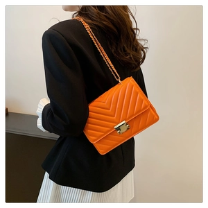 Close-up of orange quilted leather shoulder bag with gold chain and rivet buckle detail