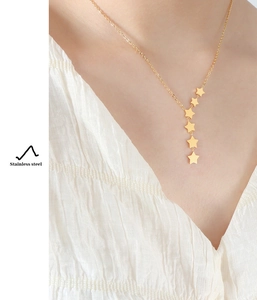 Detail view of a gold stainless steel necklace with five hanging stars worn by a model